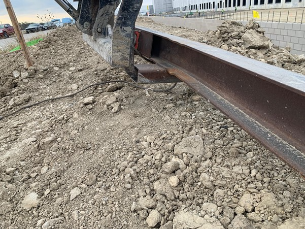 Improper forklift lifting setup using a makeshift spreader bar on a steel beam at a construction site